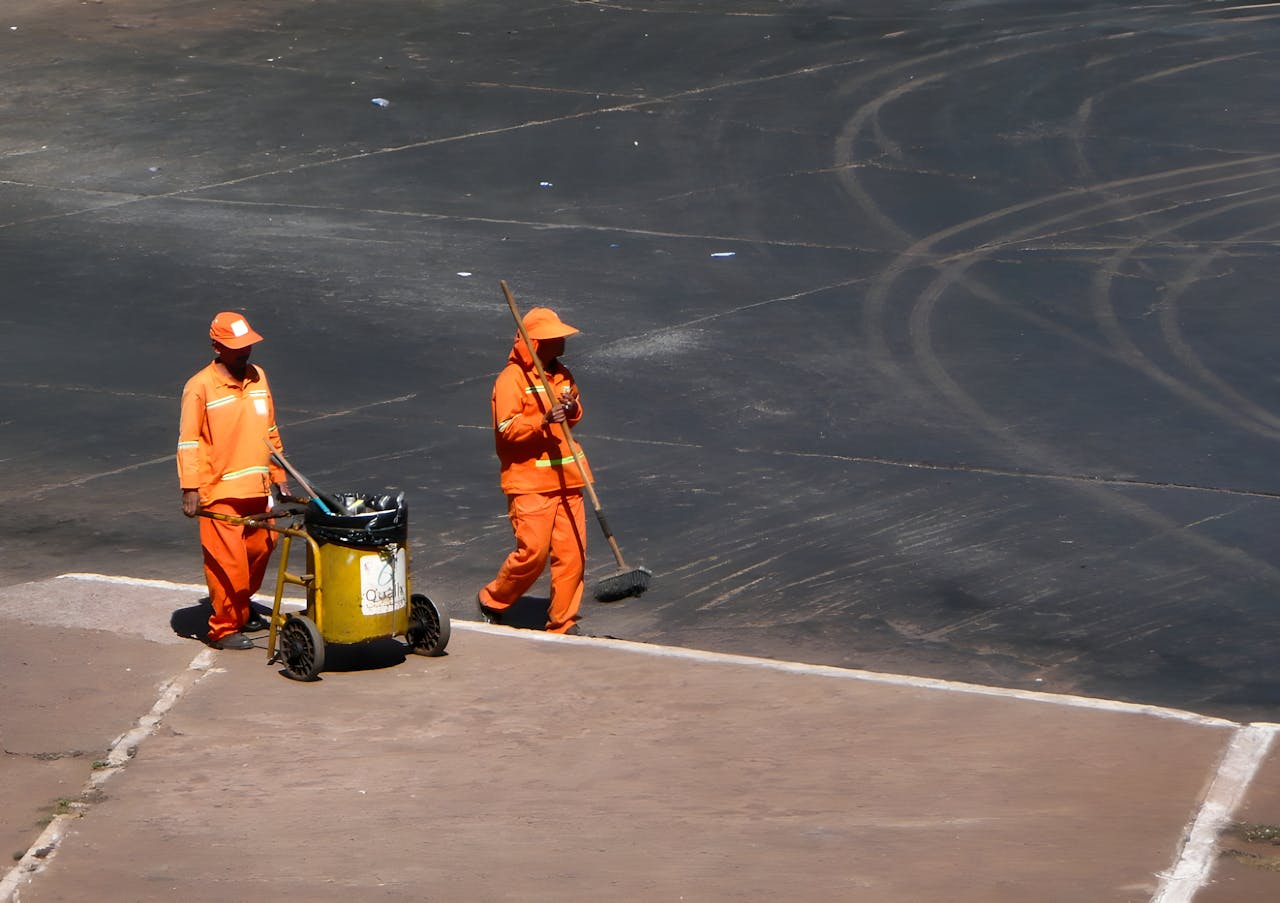 Two street cleaners working in Brasília, Brazil, wearing bright orange uniforms.